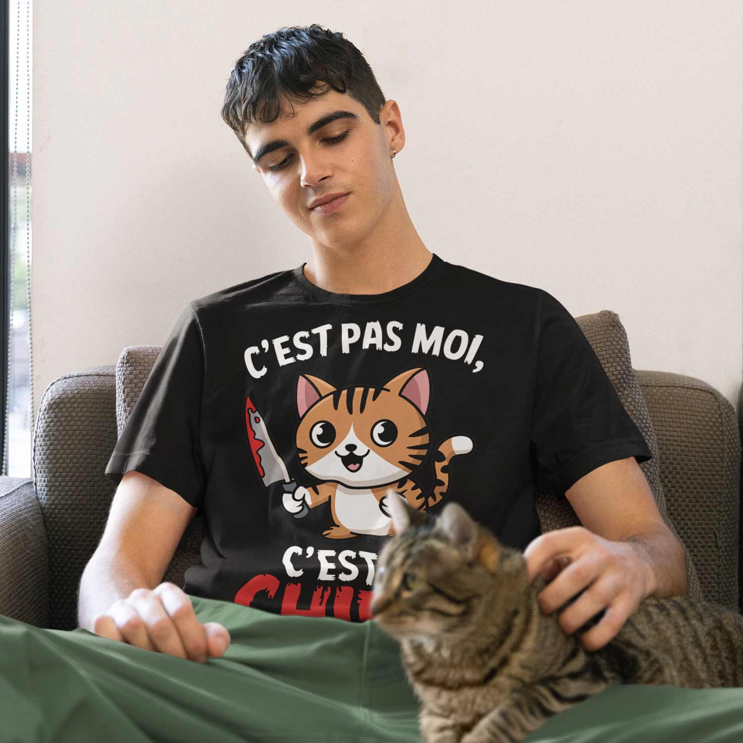 jeune homme assis avec un chat sur ses genoux portant un tshirt humour avec le design cest pas moi cest le chien