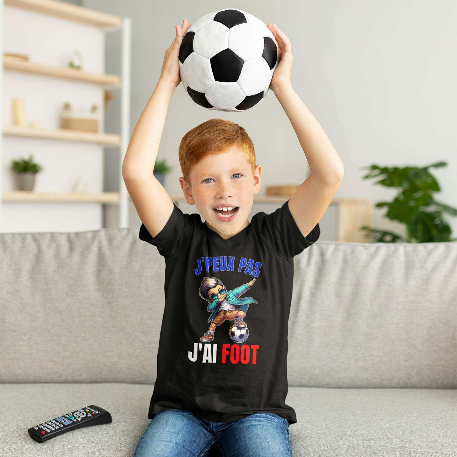 enfant assis sur un canapé tenant un ballon et portant un t-shirt avec le design “J’peux pas j’ai foot”