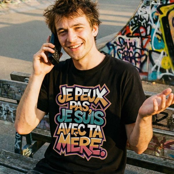 homme souriant assis sur un banc portant un t-shirt humour je peux pas je suis avec ta mère en milieu urbain